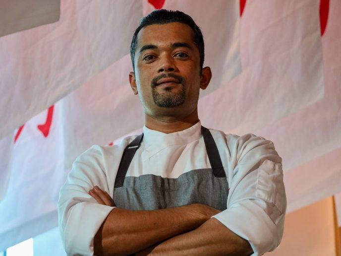 Dark haired man with arms crossed in white shirt and gray apron