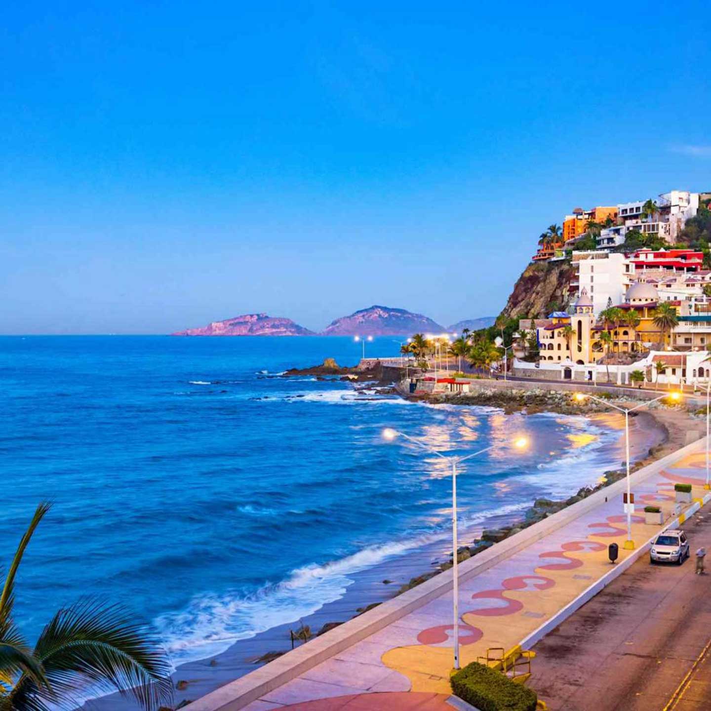 Cars drive along a road beside the ocean at dusk