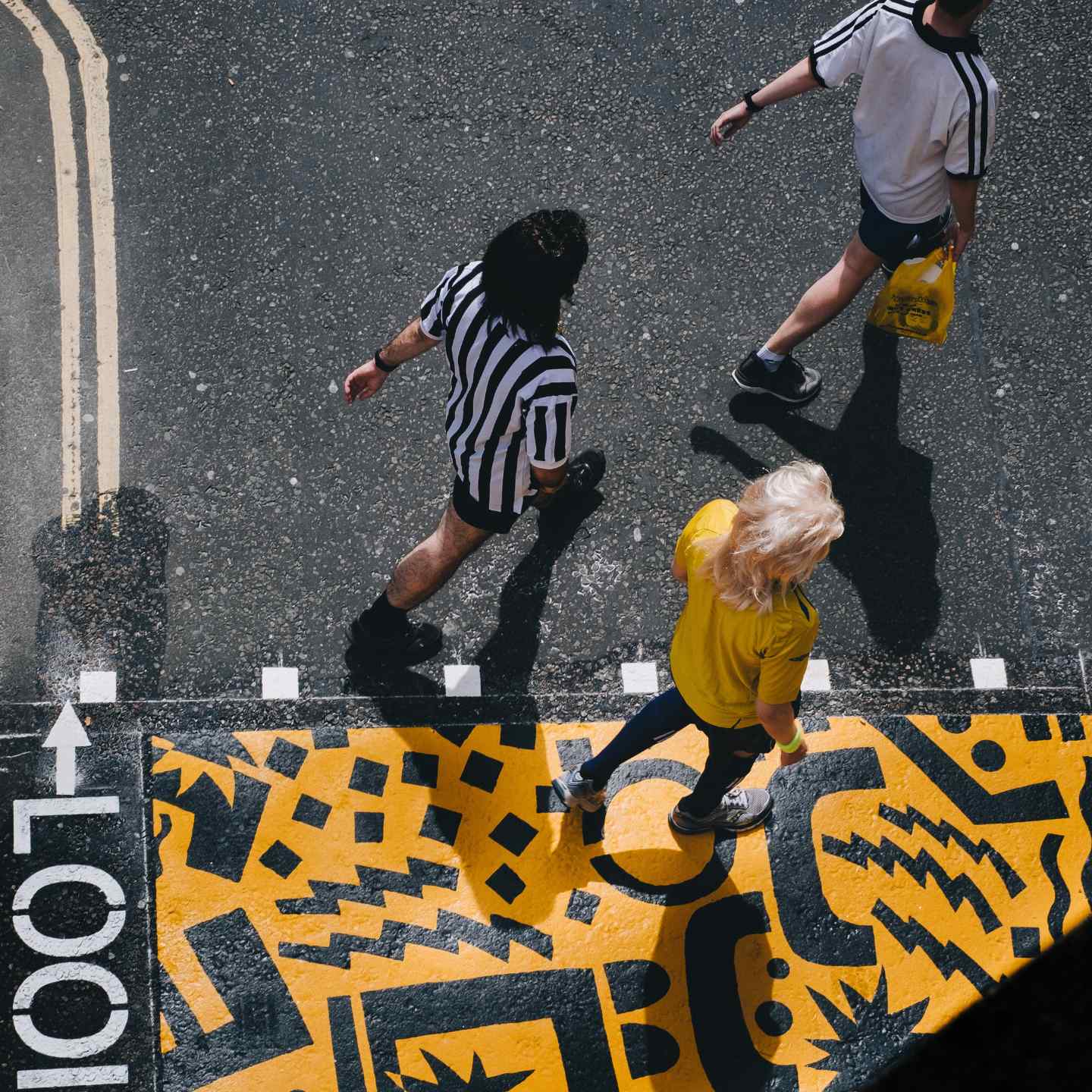 Trois amis marchant dans la rue, portant des vêtements noirs et blancs, avec du street art jaune et noir sur le sol