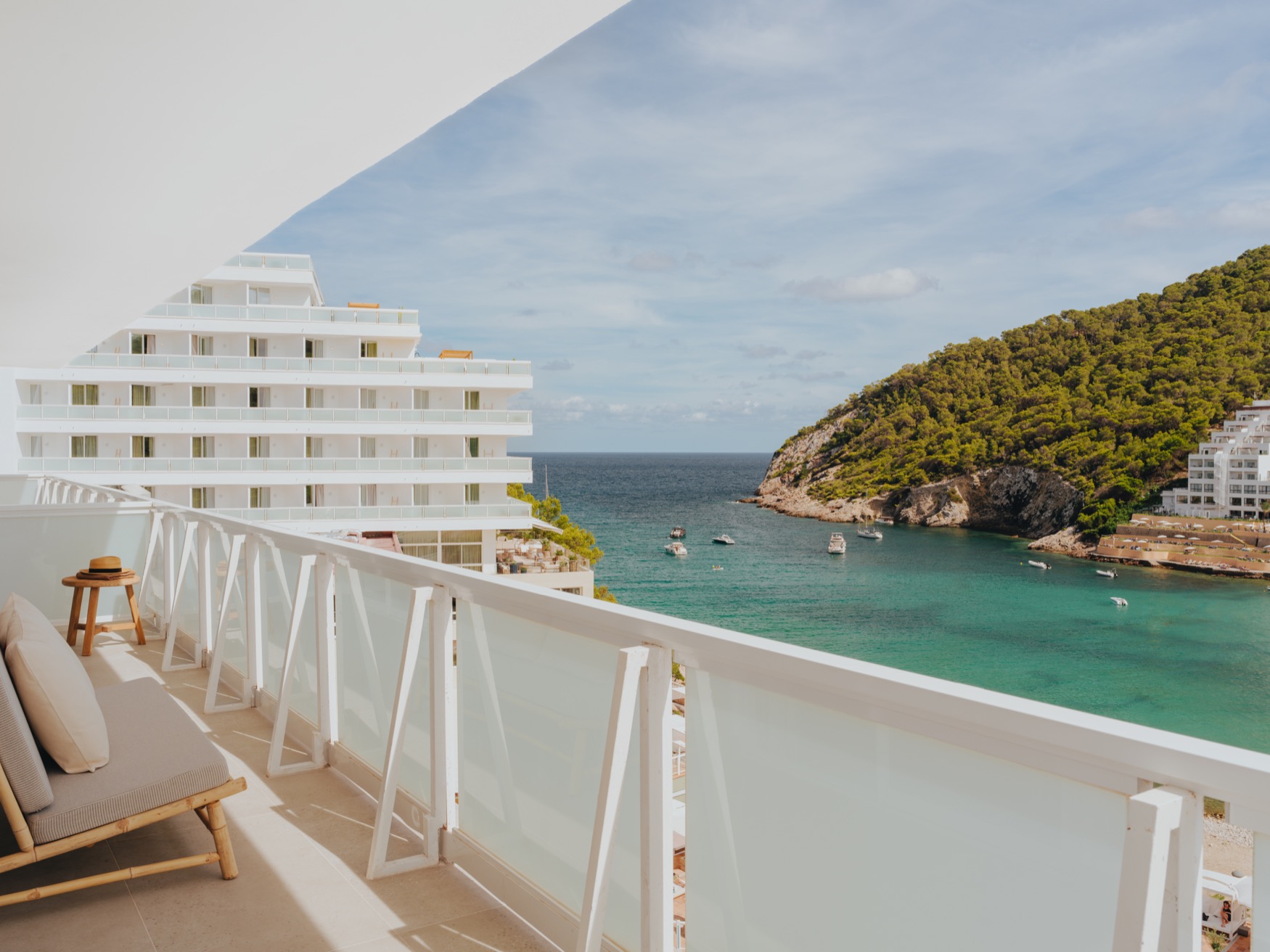 Balcon avec fauteuil et vue sur la mer, les collines vertes et une partie des bâtiments de l'hôtel