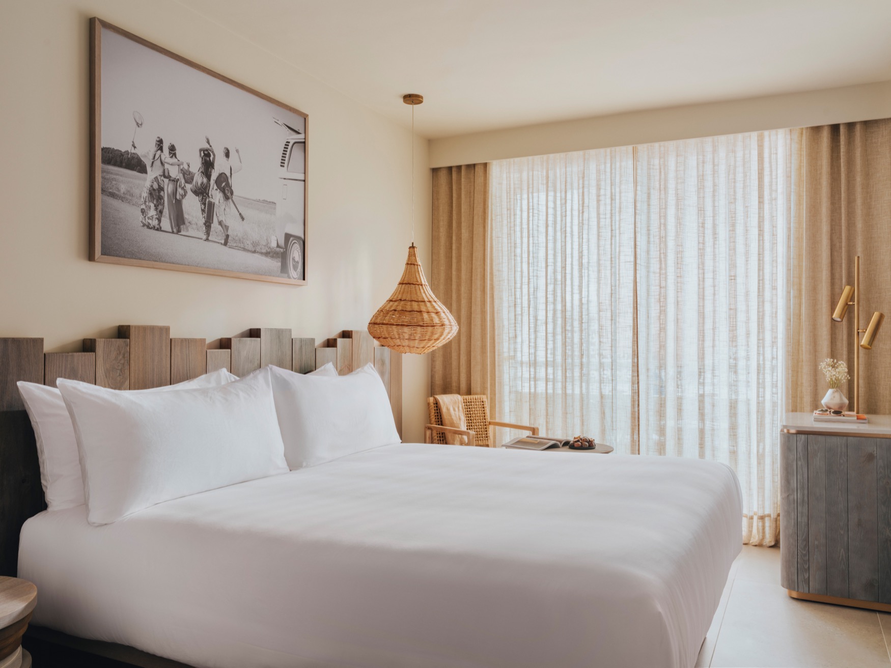 A double bed at the forefront with armchair and small table next to the bed, and console table with a lamp on top to the right