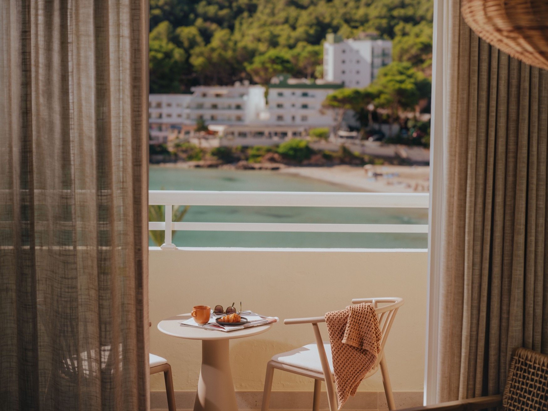 A view of a balcony with two chairs and a coffee table, displaying a view of the sea and the beach with hotels in the background