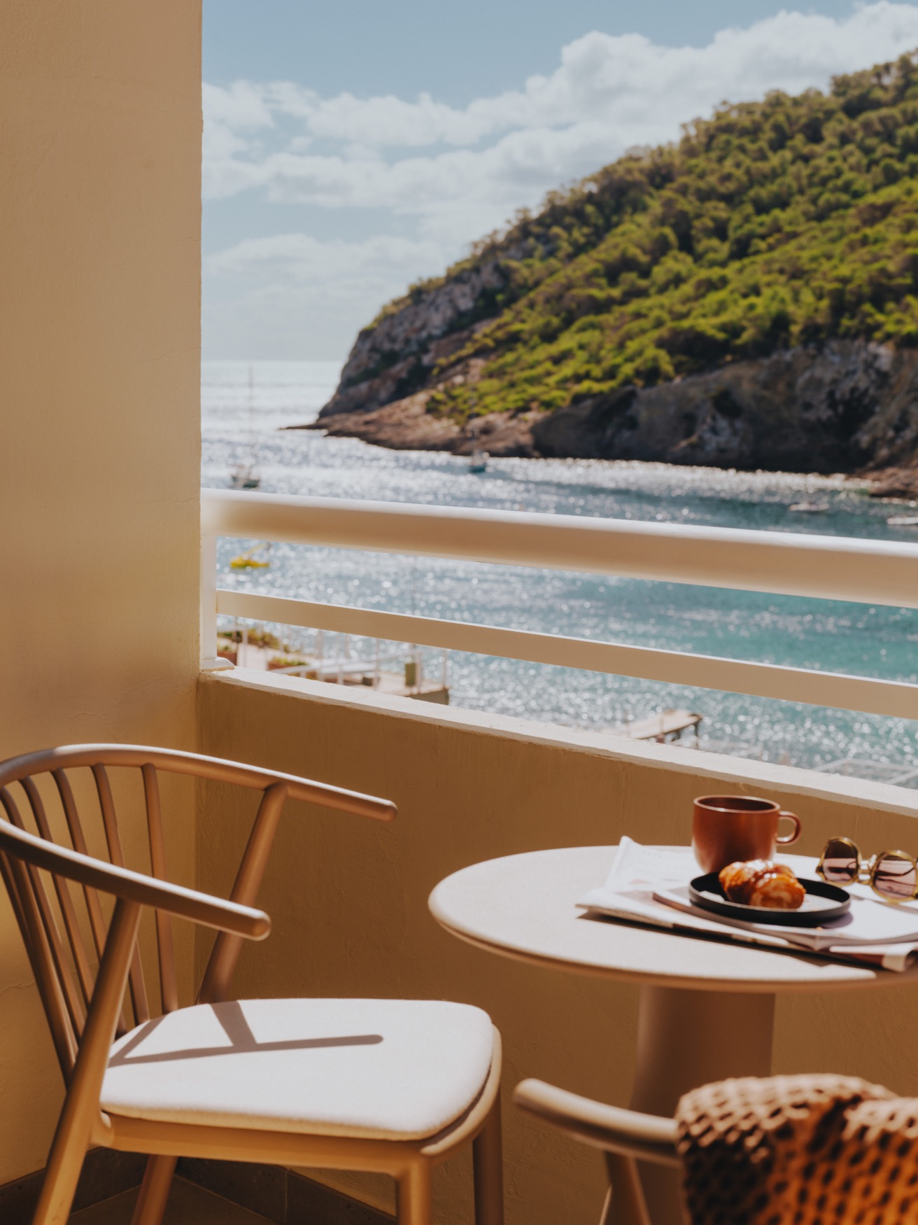 A chair and a coffee table on the balcony displaying sea views and green hills