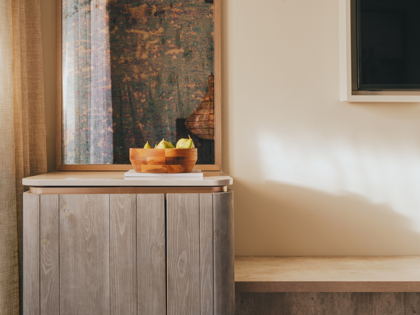 A vanity table with wall mirror on the left showing a part of a bench and wall hanged TV on the right