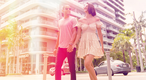 Couple walking holding hands in front of high rise building with palm trees in background