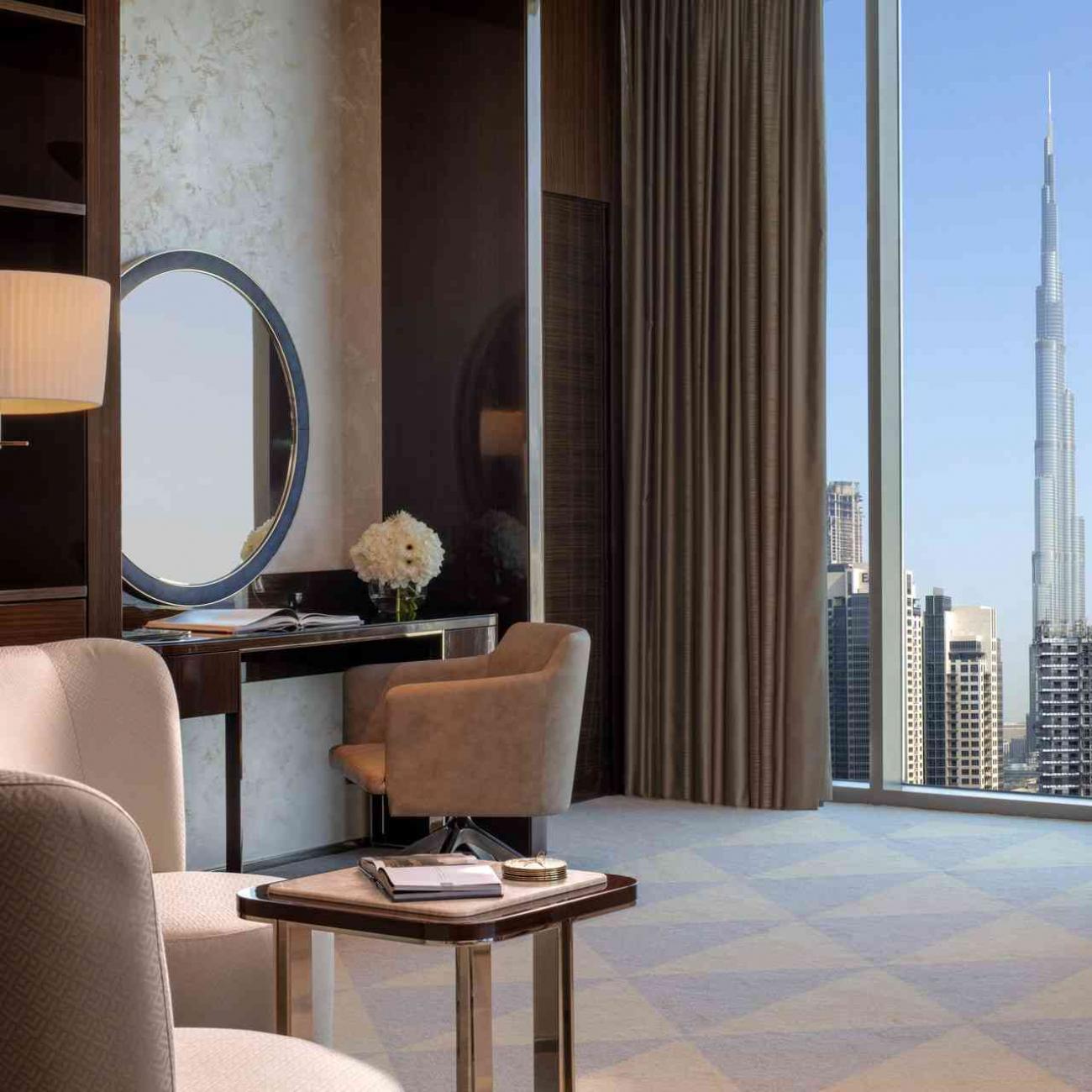 Two occasional chars and a coffee table at the forefront, small console with mirror to the left and a city view of Dubai and Burj Khalifa building on the right