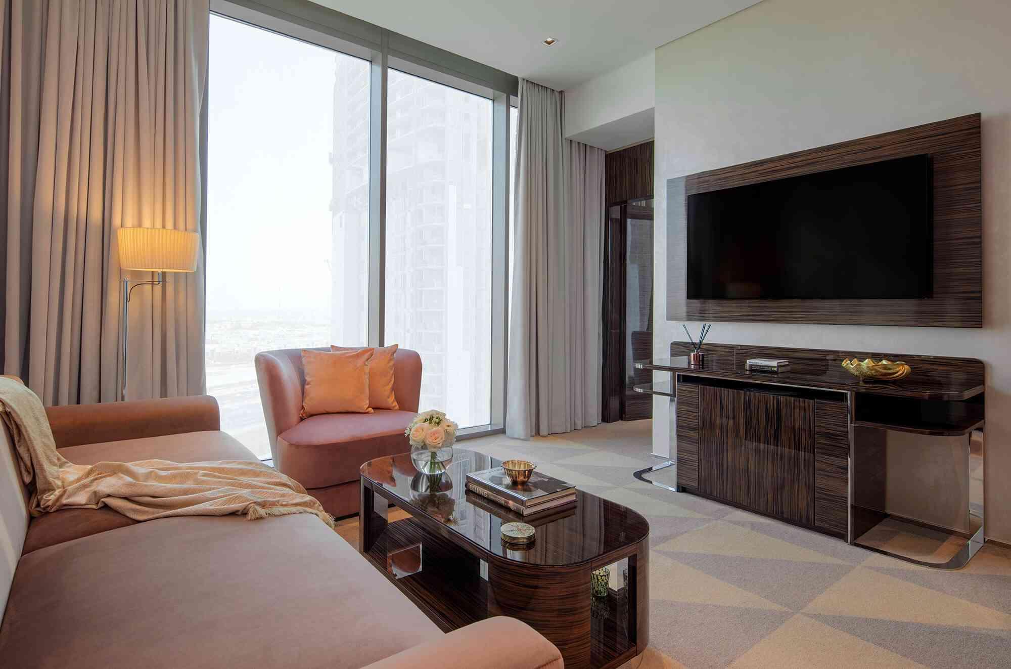 A dark beige 2 seater sofa with a coffee table, an armchair in the forefront, and a wall mounted TV and console table