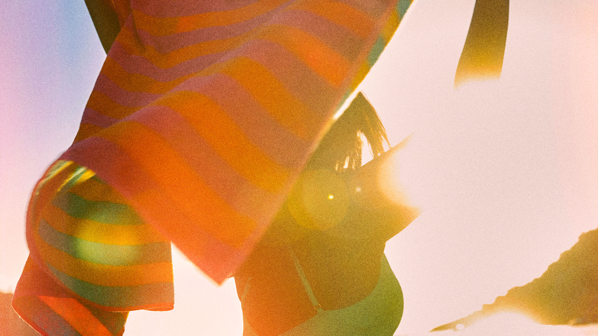 Orange and pink striped towel held overhead by woman in blue bathing suit