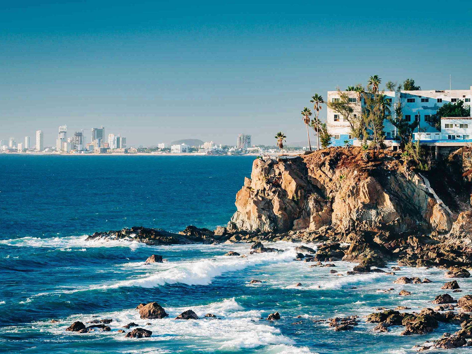 Falaises plongeant dans un océan d'un bleu profond avec une ville dans le lointain