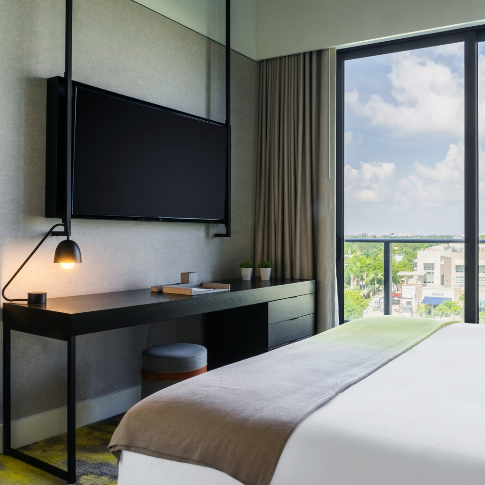 Bottom of a hotel bed showing large TV on the wall, above desk area