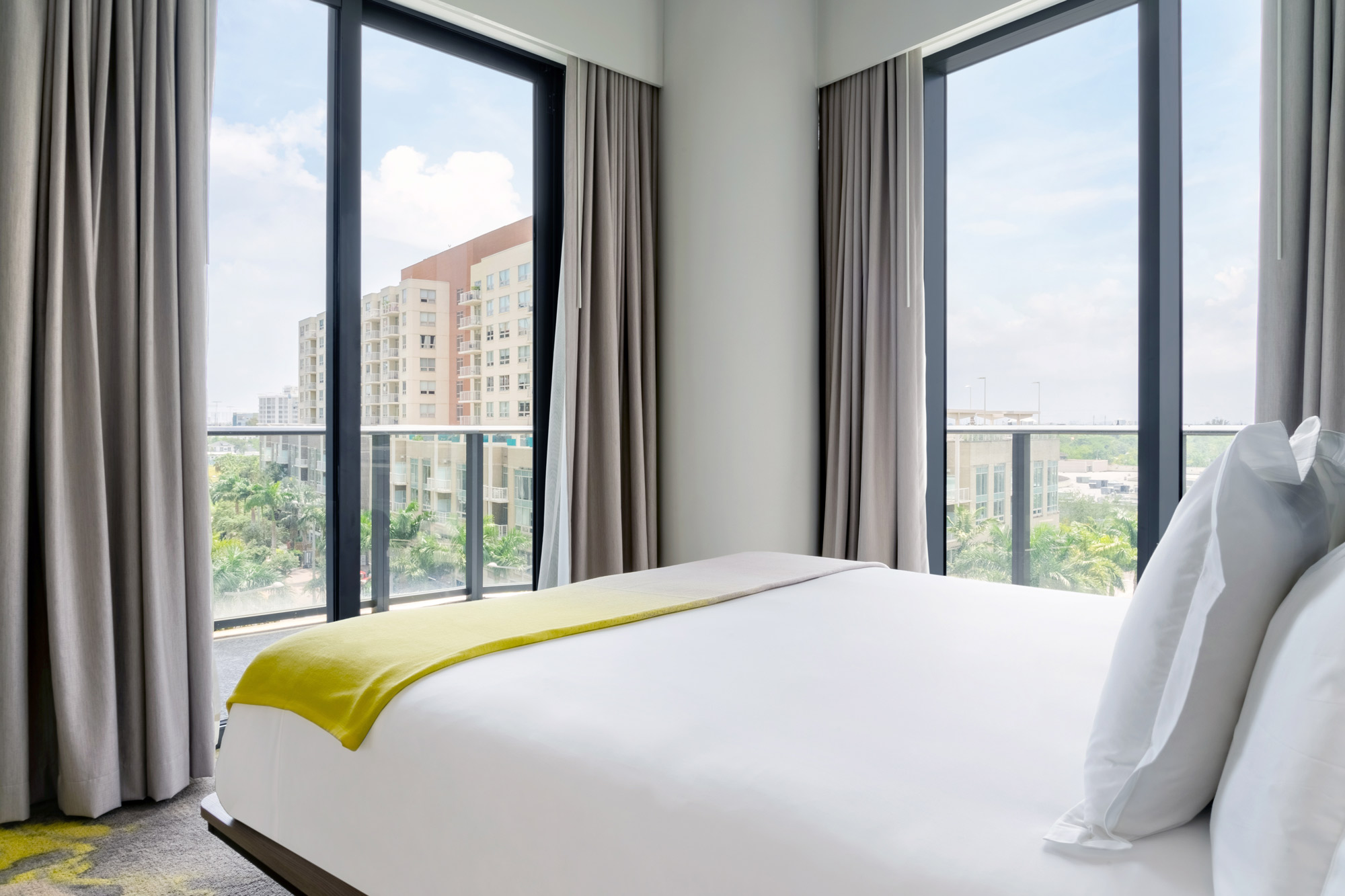 Hotel room with large double bed in front of big windows on two adjacent walls, showing views of the surrounding area