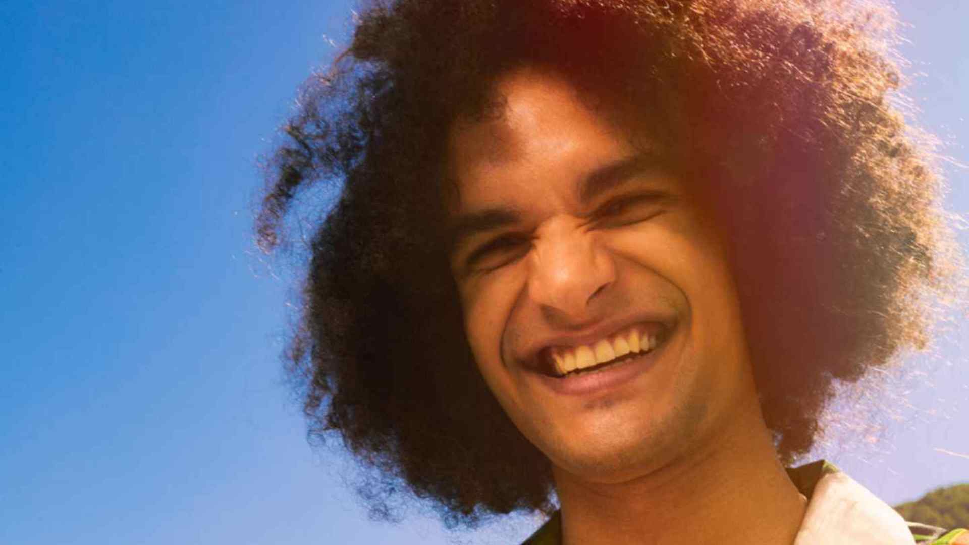 Homme aux cheveux bouclés souriant avec un ciel bleu en arrière-plan