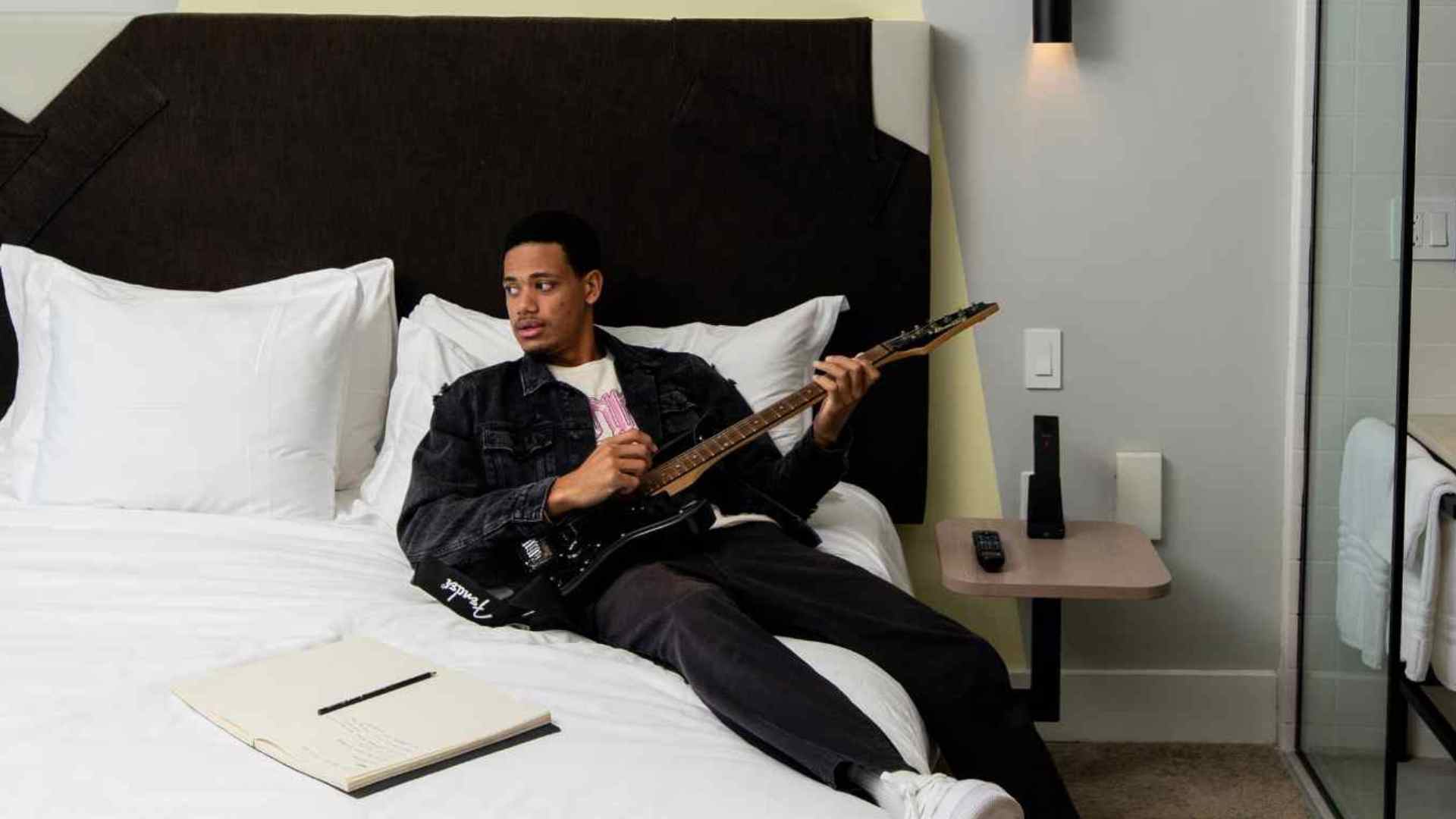 Homme allongé sur un lit blanc tenant une guitare noire