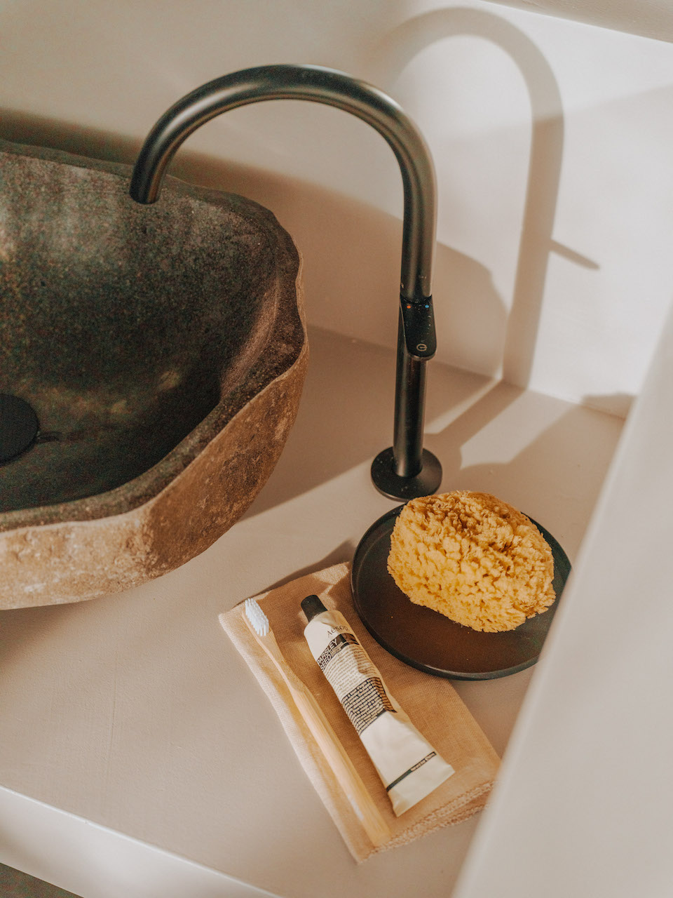 Close up of stone bowl sink and black faucet on beige countertop with soap and lotion