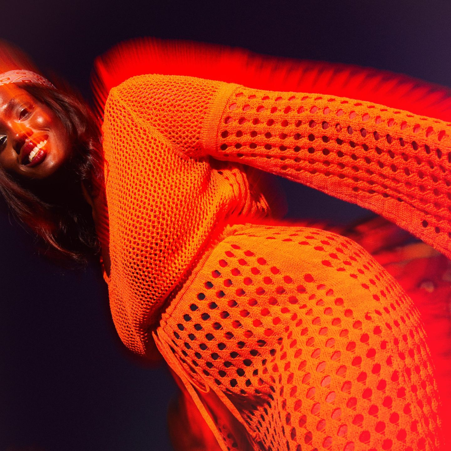 Woman in orange dress smiling at the camera with a dark background behind her.