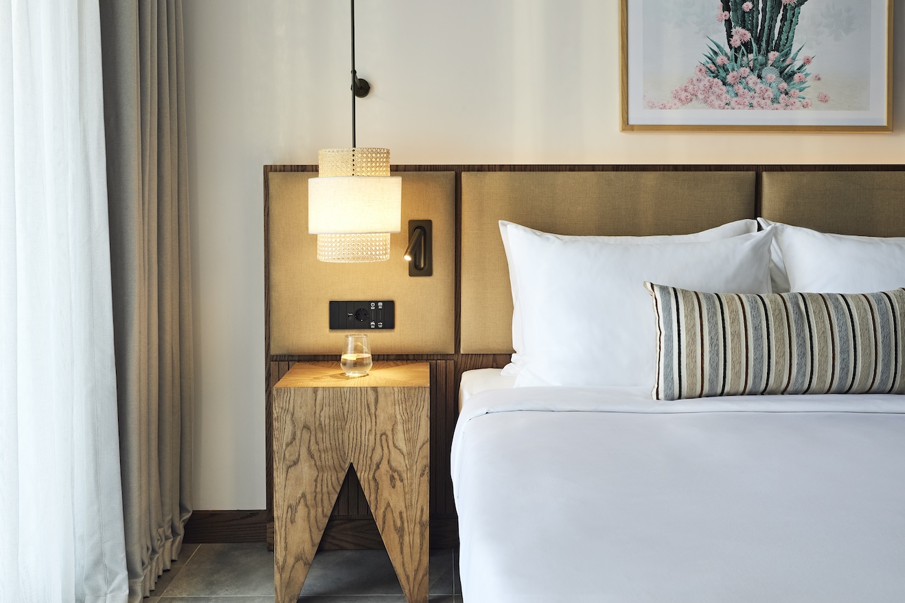 Large white bed with beige headboard and beige bedside table with pendant light overhead