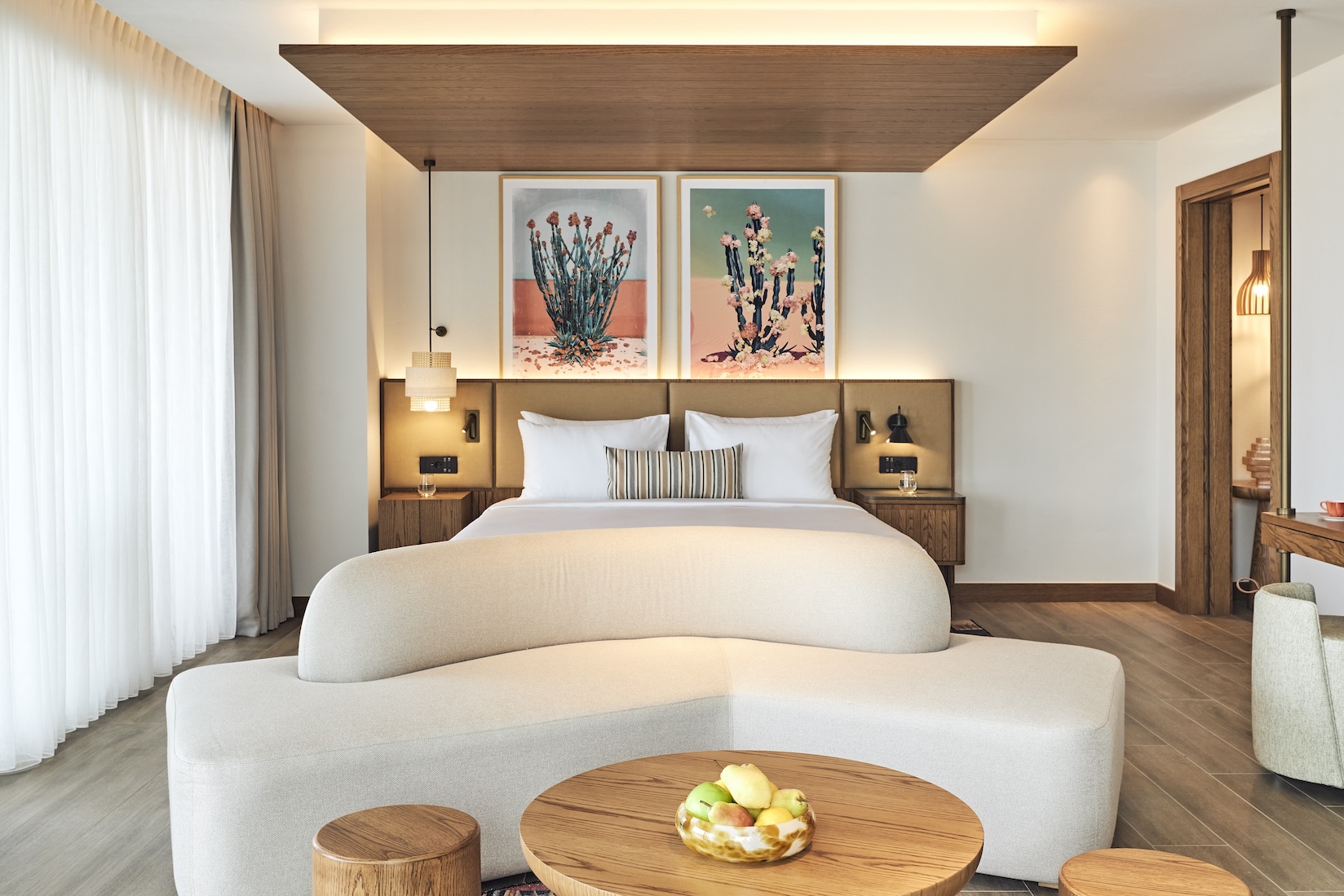 Large white bed with headboard and cream sofa at the end of the bed and small wooden coffee table with small stools