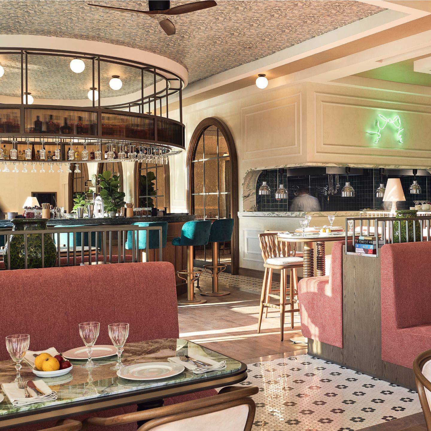 Dining room with pink booths, patterned tile floor, and circular bar with velvet turquoise bar stools