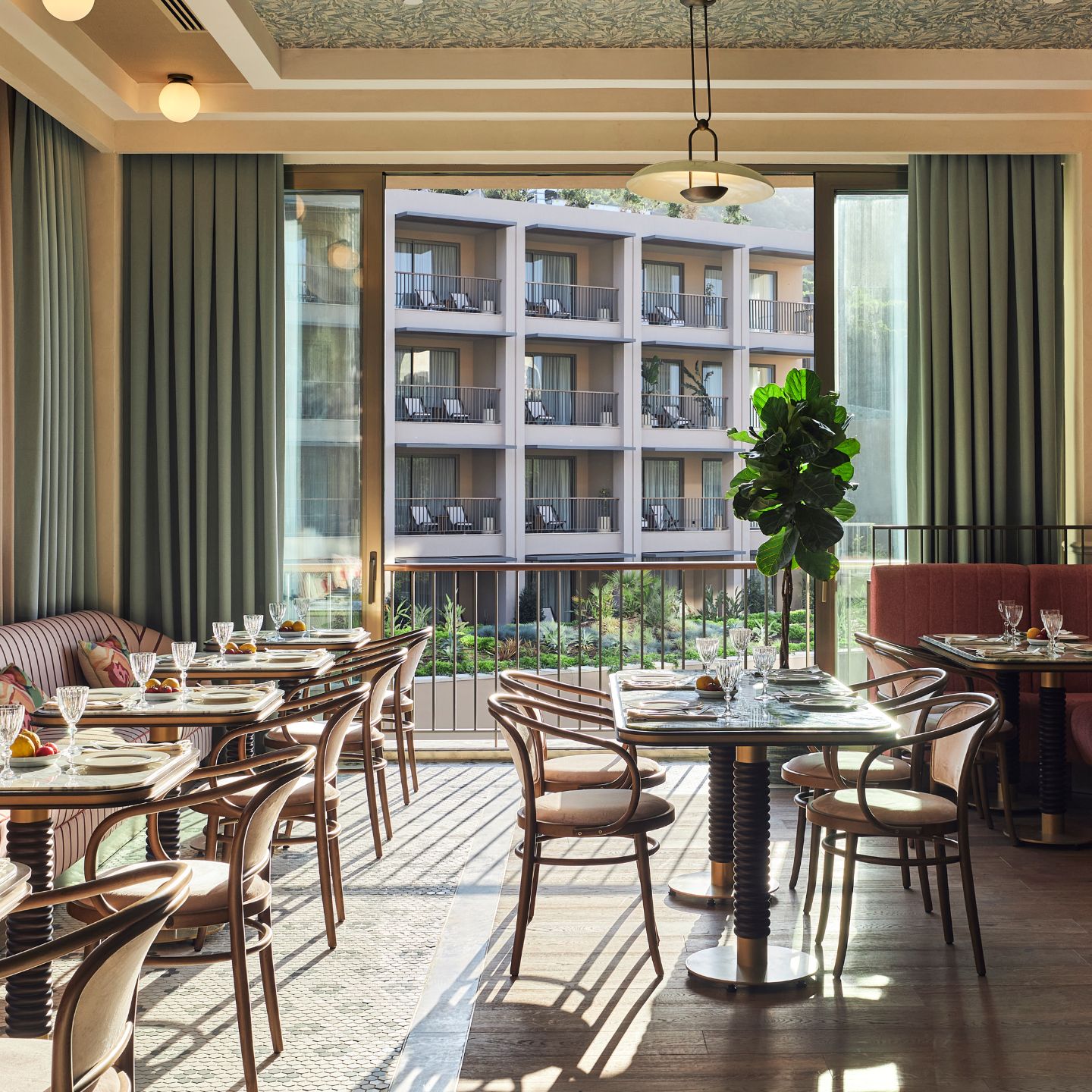 Dining room with multiple small tables and chairs and seafoam green curtains covering a large window looking out to another building