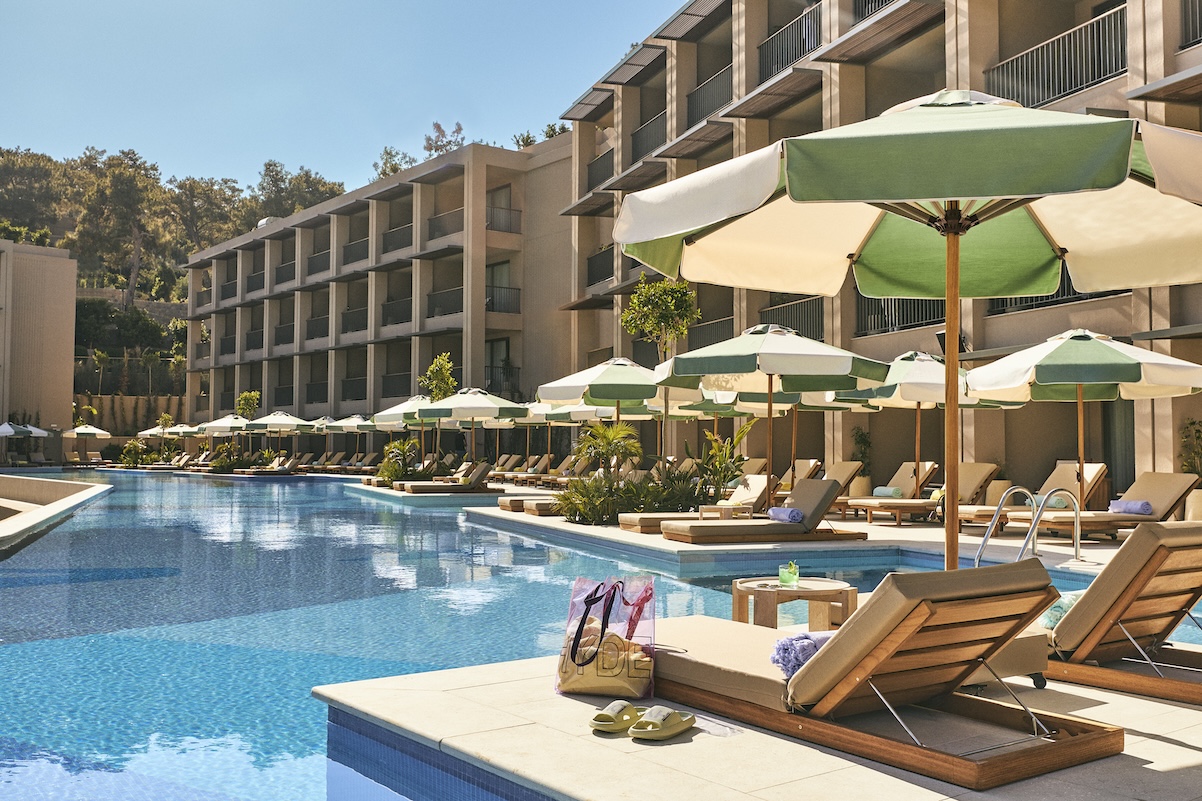 Blue pool with row of chaise lounge chairs, green and white striped umbrellas, and beige building in the back