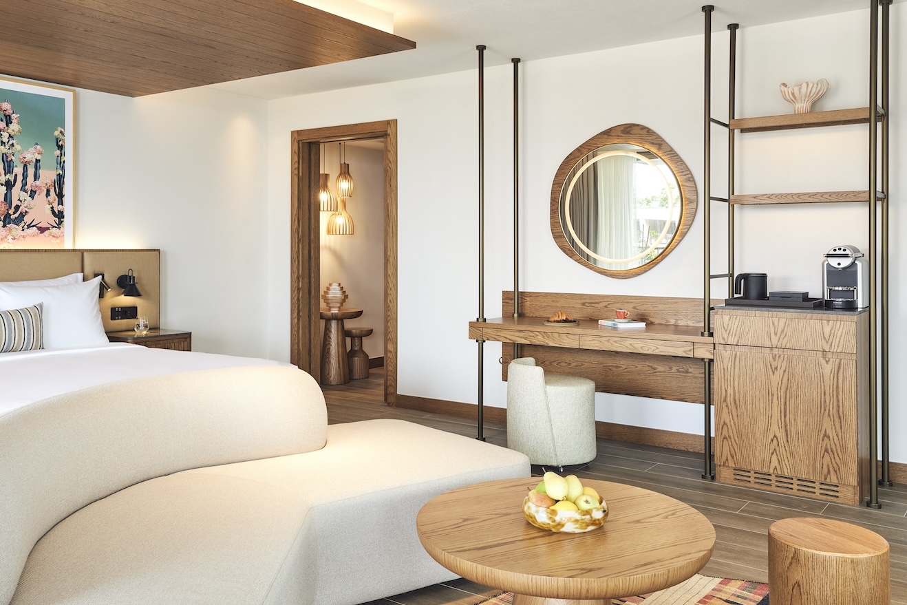 Corner of a large bed with cream sofa at the end and wooden vanity and mirror to the side