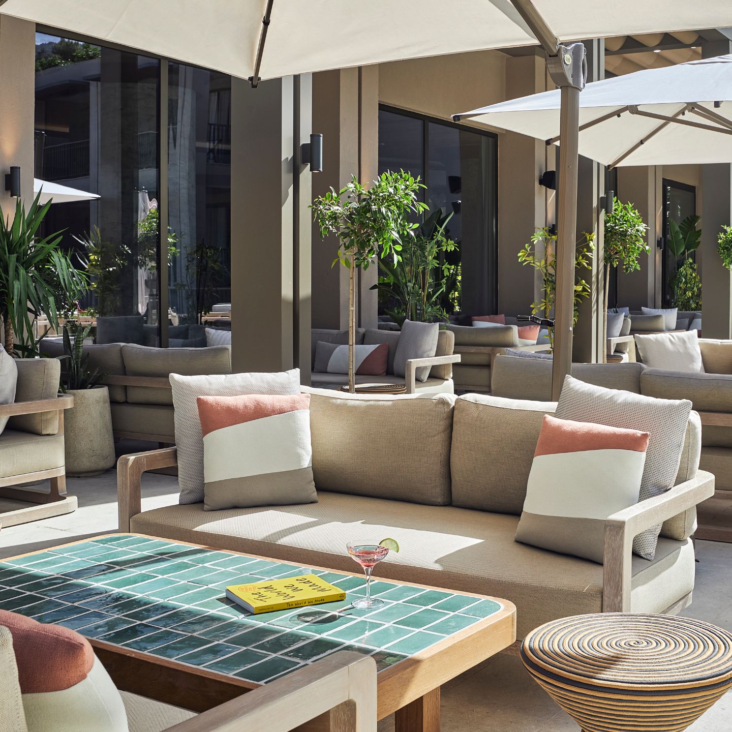 Outdoor patio with beige sofa and pillows, turquoise tiled coffee table, and umbrella up above