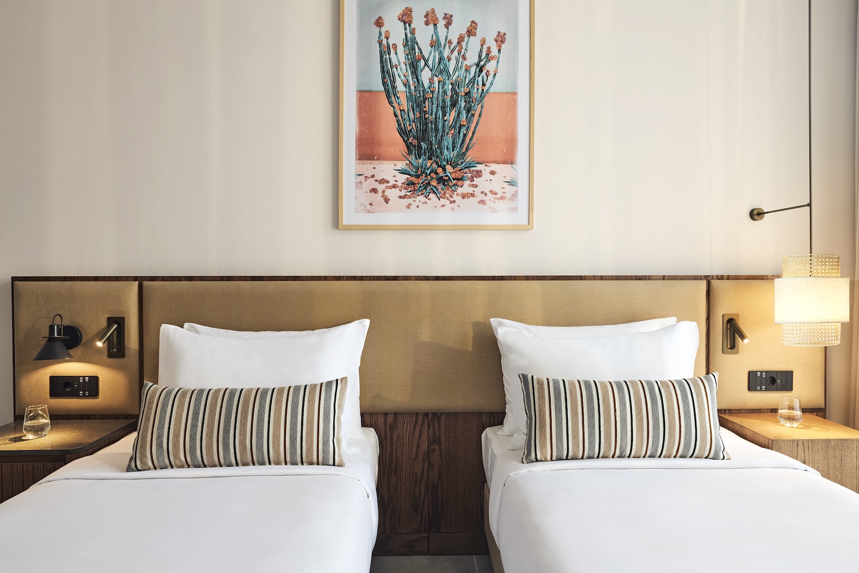 Twin beds with matching throw pillows and a beige headboard with a framed painting on flowers on the wall above