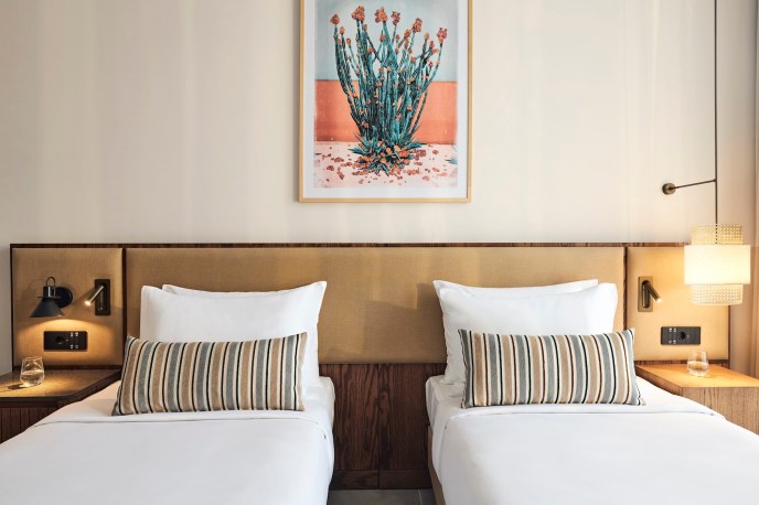Twin beds with matching throw pillows and a beige headboard with a framed painting on flowers on the wall above