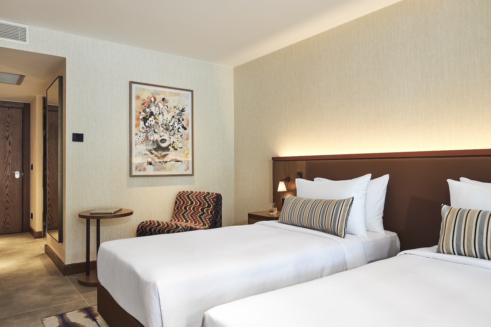 Angled view of two twin beds with burgundy headboard, patterned chair in the corner, framed art on the wall