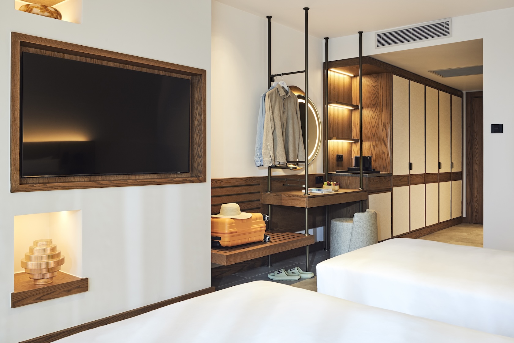 The ends of two white twin beds facing a wall with a plasma screen tv