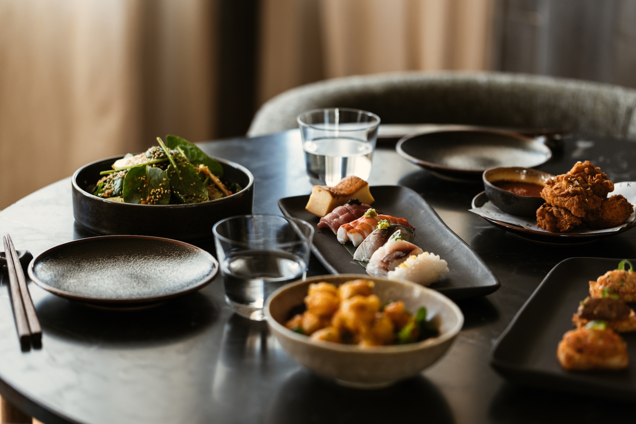 Image of dark table with multiple different dishes on it with glasses of water and chopsticks