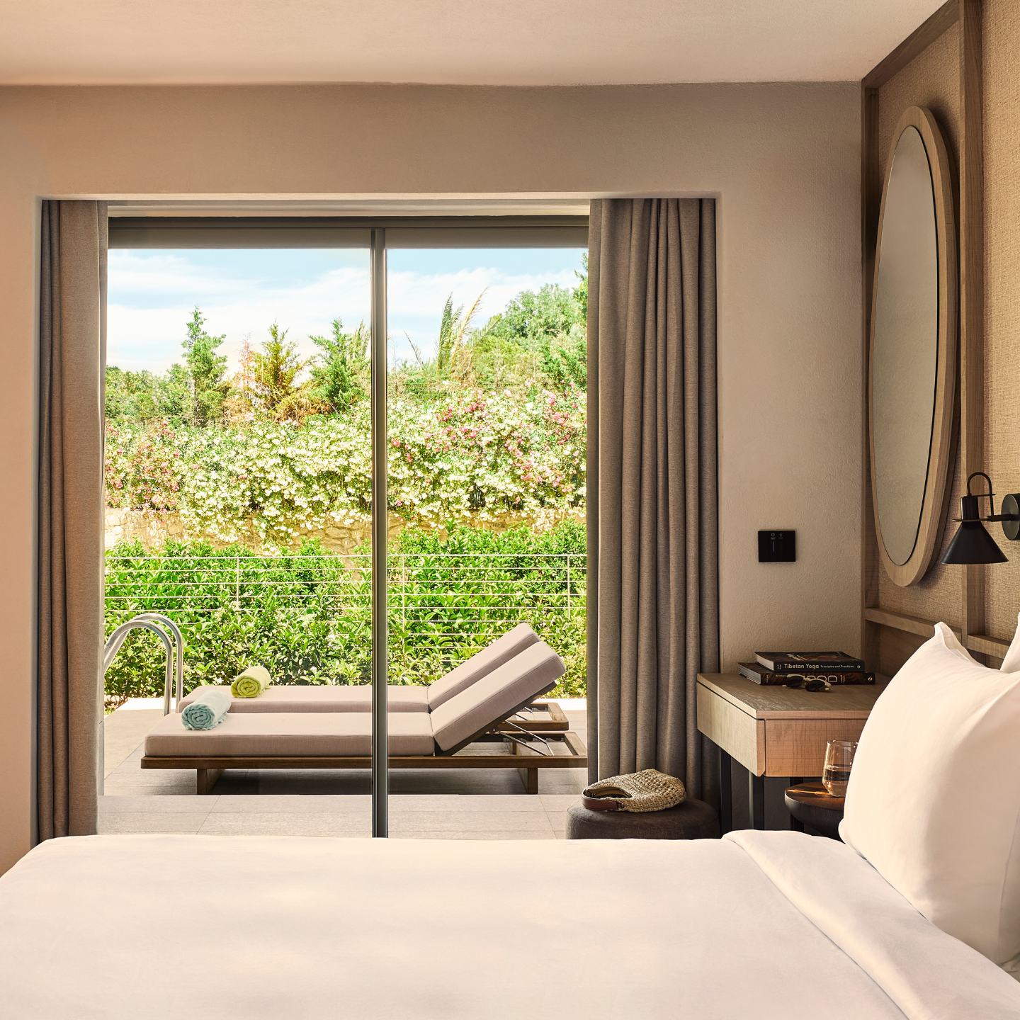Modern hotel room overlooking a deck with sun loungers and plenty of greenery behind