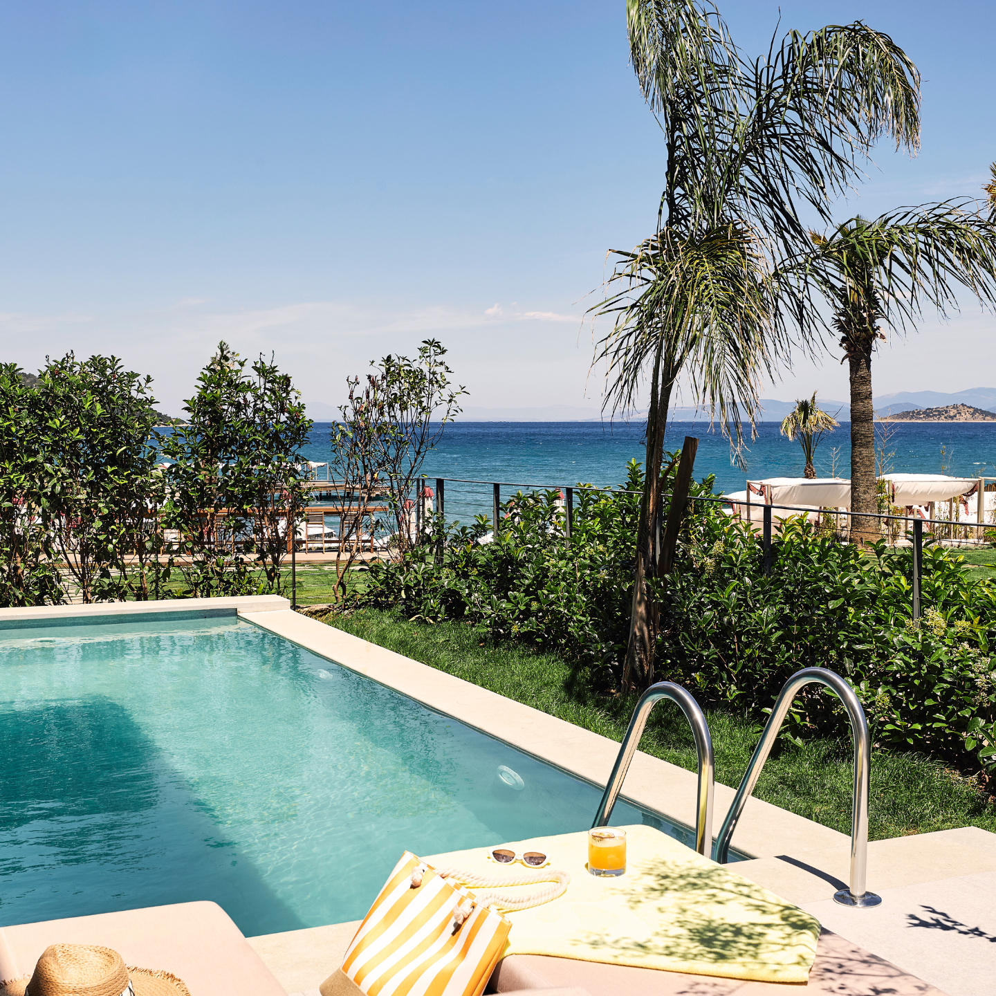 Bright blue color pool with sun lounger overlooking the sea, palm trees and beach