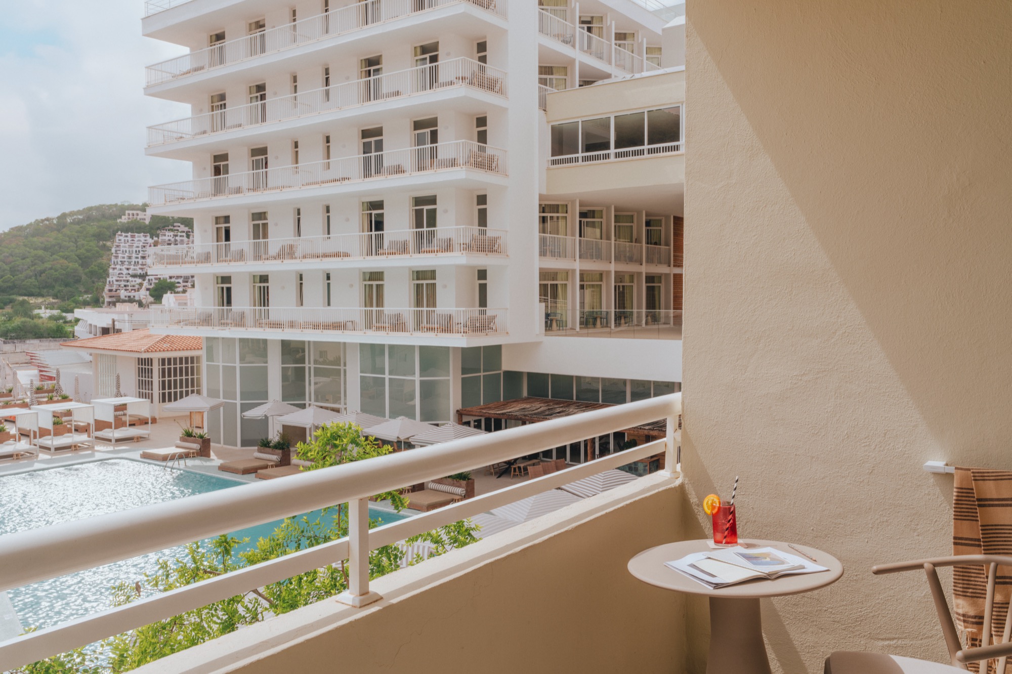 Chairs and a table on a balcony overlooking a swimming pool and more hotel rooms