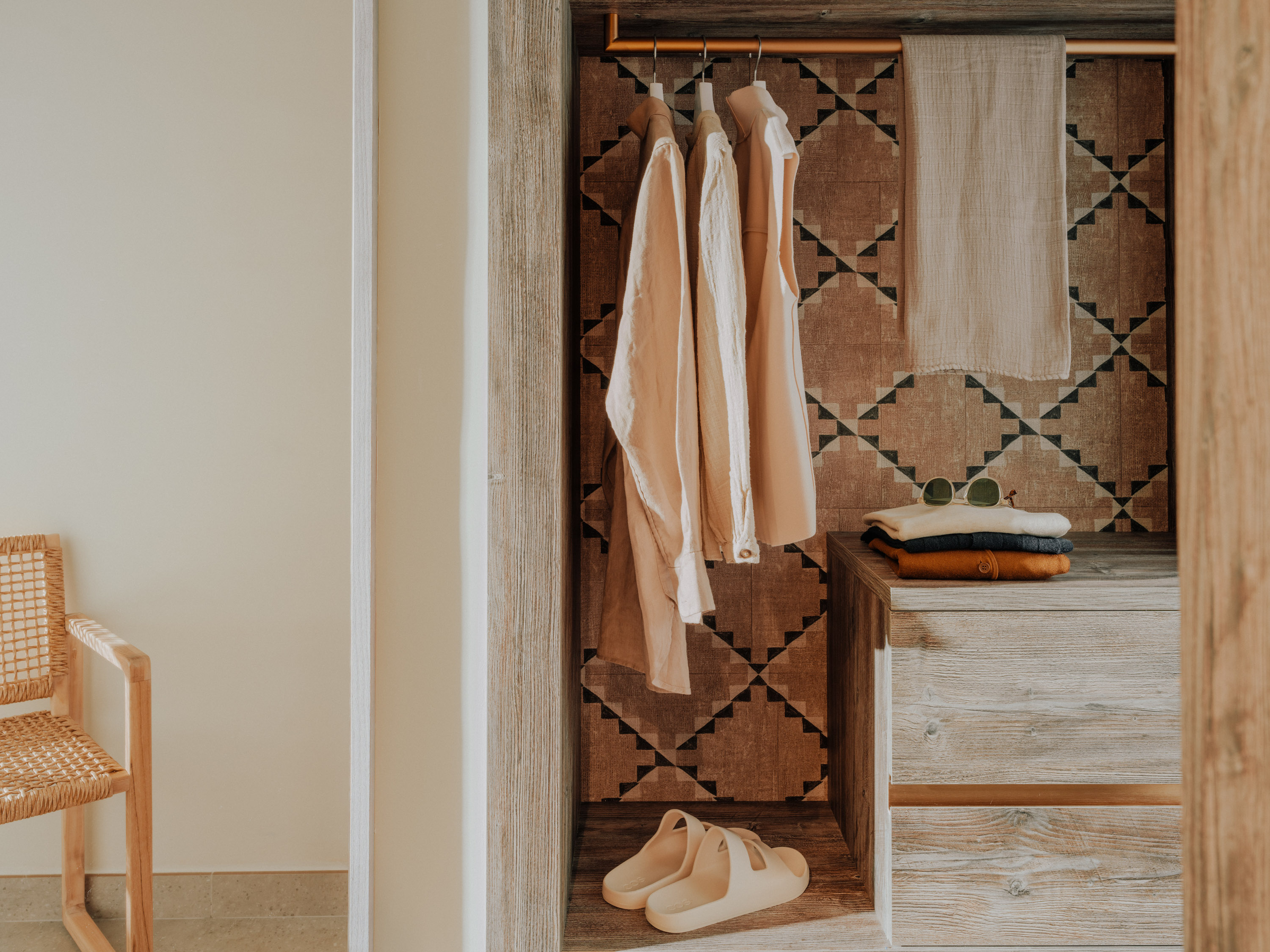 An open wardrobe with clothes hanging and folded, with sandals on the floor