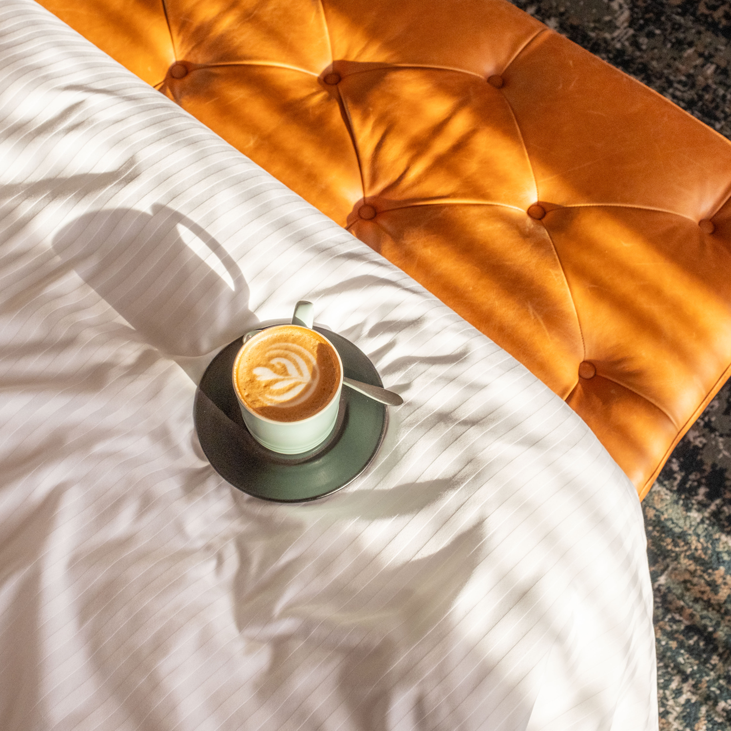 A cup of coffee placed on the bed, with sunlight shining through on to the bed.