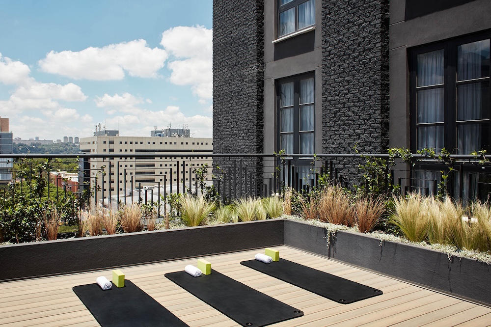 The stretch studio, out on an open balcony, with three black yoga mats, three white towels wrapped, and a block placed on each yoga mat.