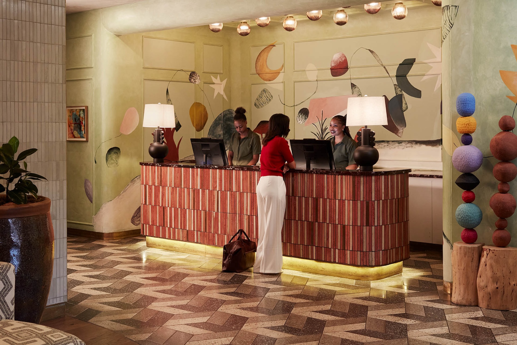 A girl in a red top and white pants checking in at Hyde's reception, with our ladies giving our guest a warm welcome.