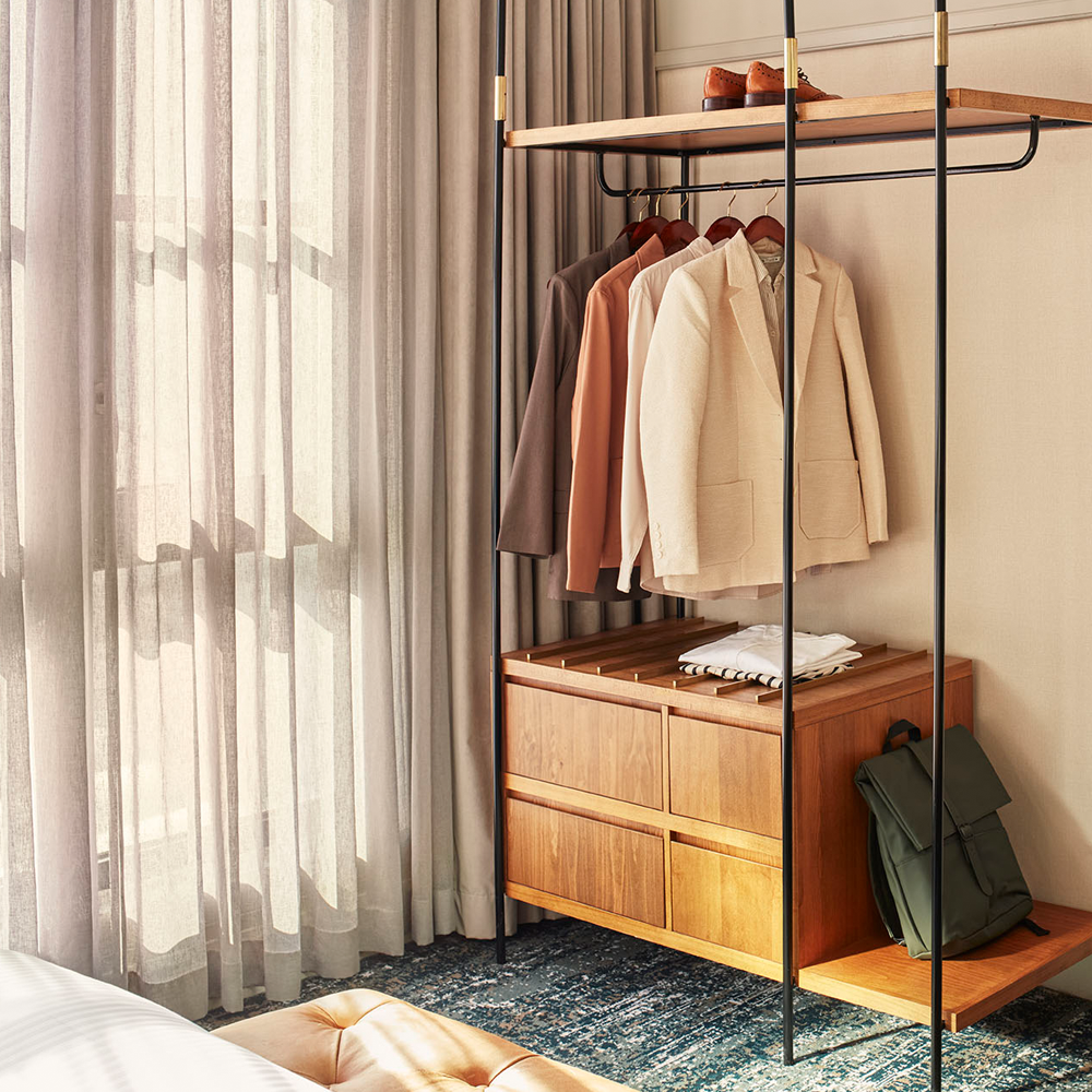 Natural sunlight shining through the curtains, and the open wooden wardrobe with drawers at the bottom.