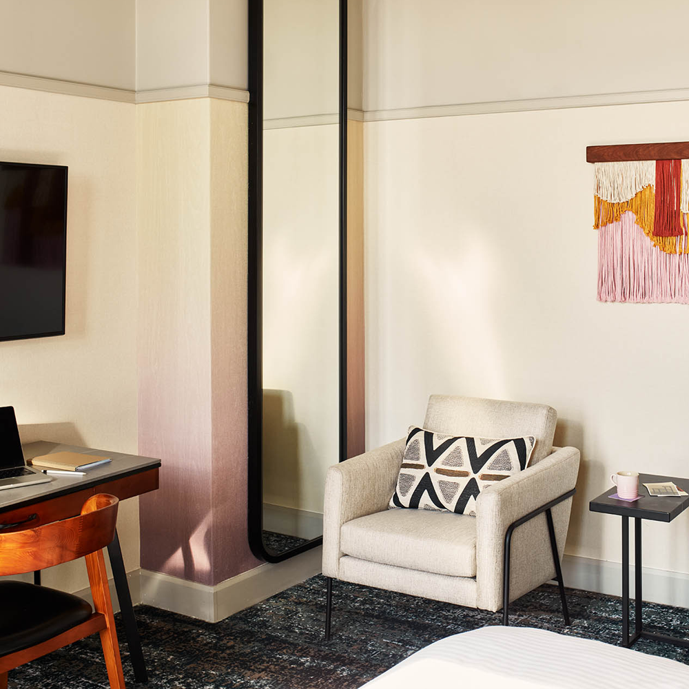 a grey 1-seater couch, with a side-table placed next to the couch, and a full-length mirror on the opposite side of the 1-seater couch.