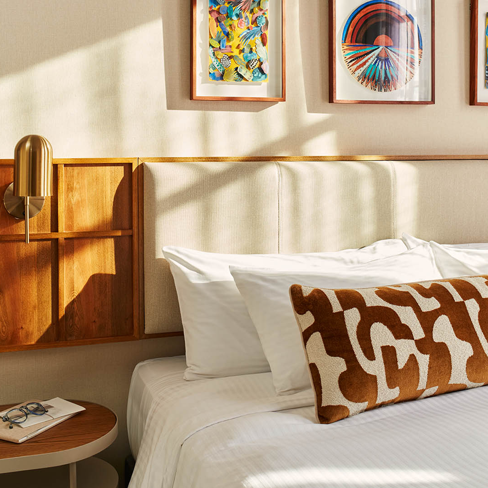 A well-lit, close-up image of the king-sized bed, with art pieces hanging on top of the bed, and the cream headboard.