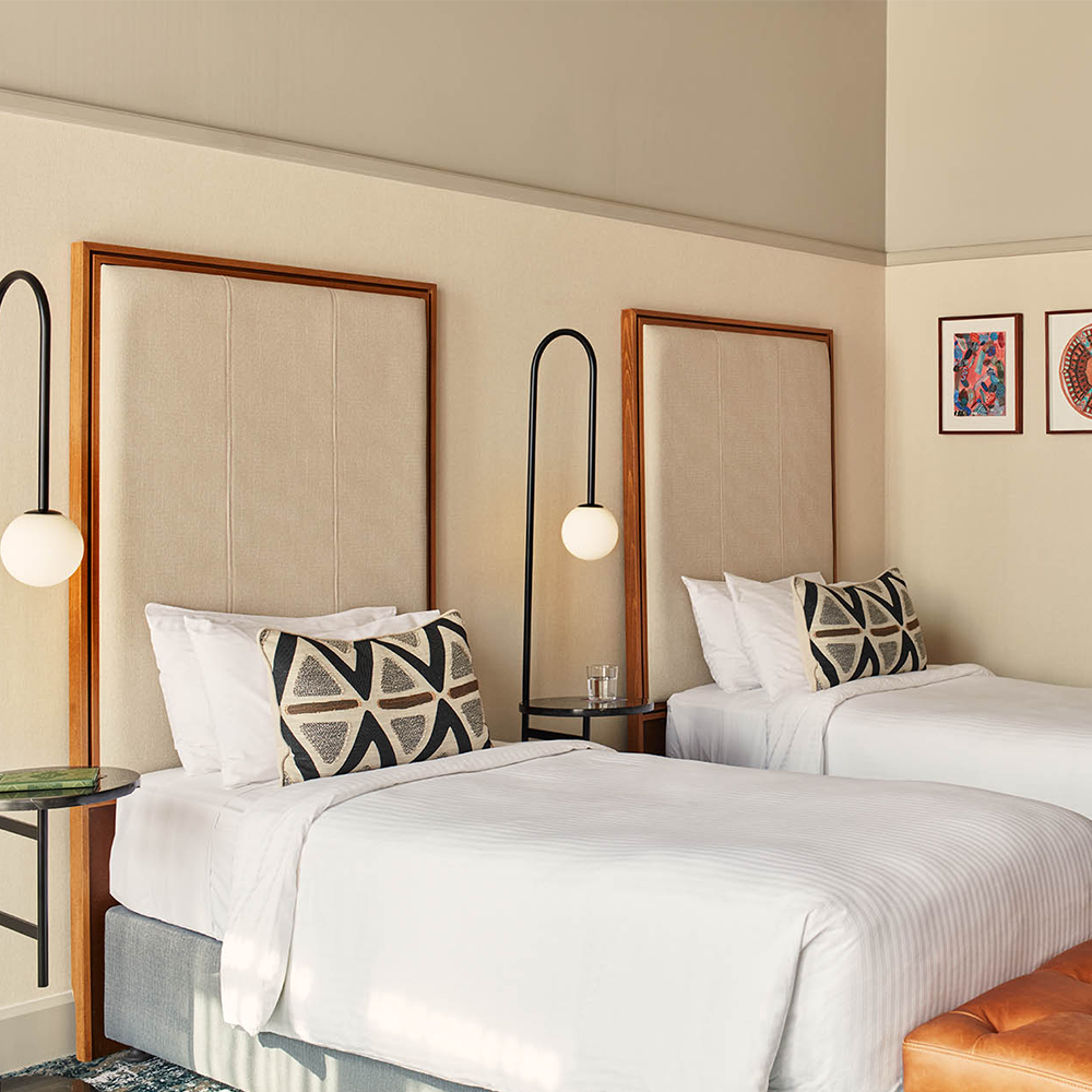 Two twin beds, each with a lamp next to the bed, and art pieces to the right of the wall.