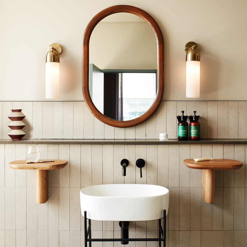 A white sink, with shelves on either side, and a mirror on top of the sink, with a light on each side.