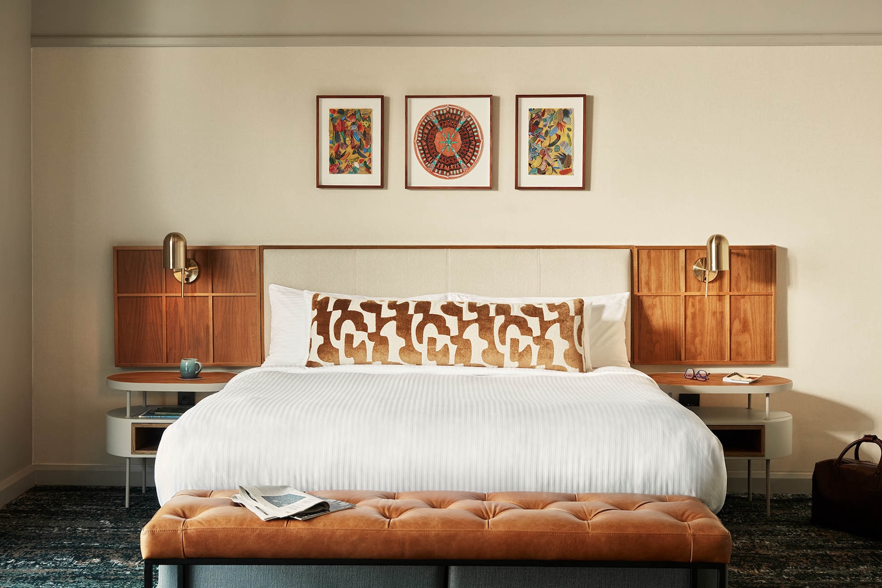 A king-sized bed, with a cream headboard, and three art pieces on top of the bed.