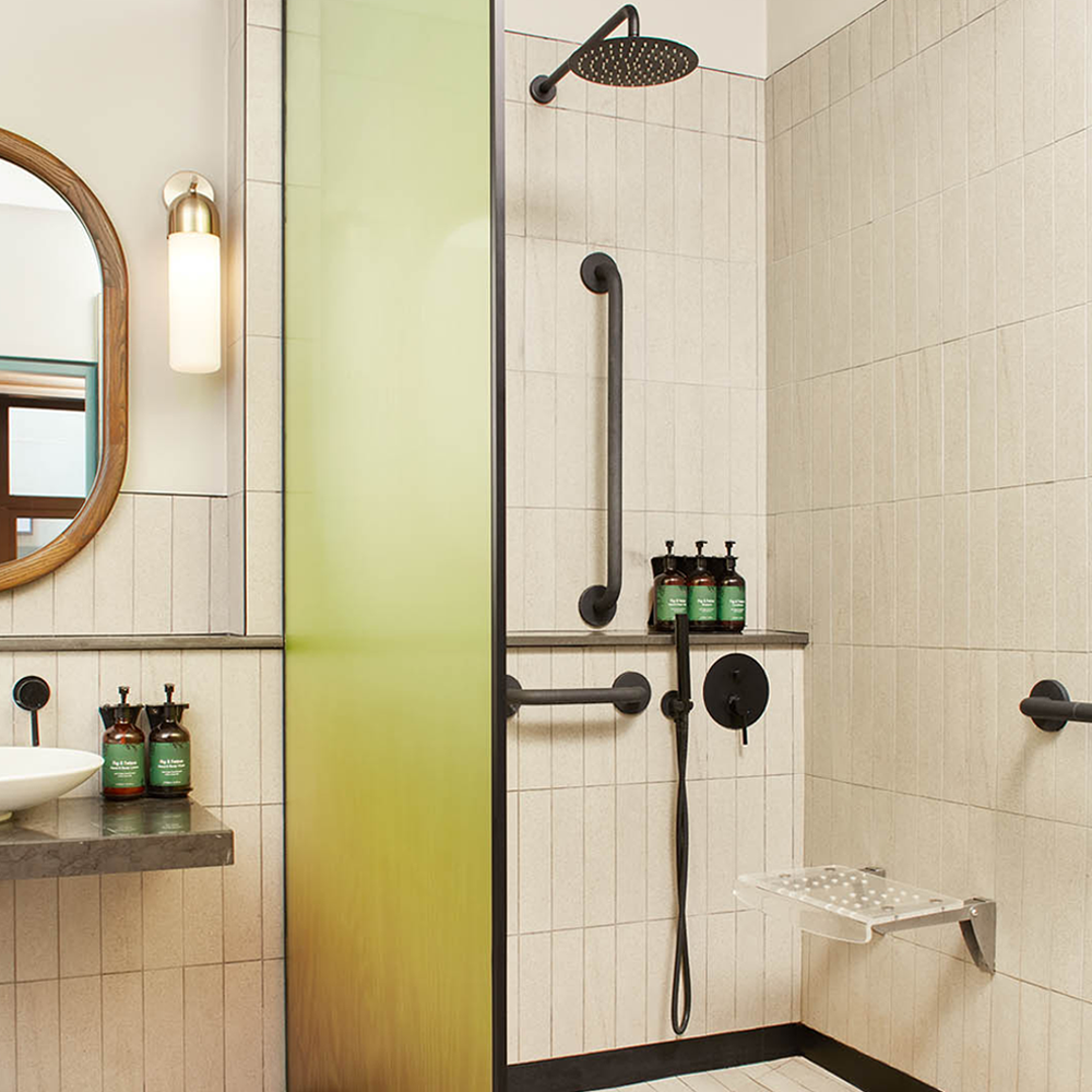 A wheelchair accessible walk-in shower, with handles, and a seat in the shower.