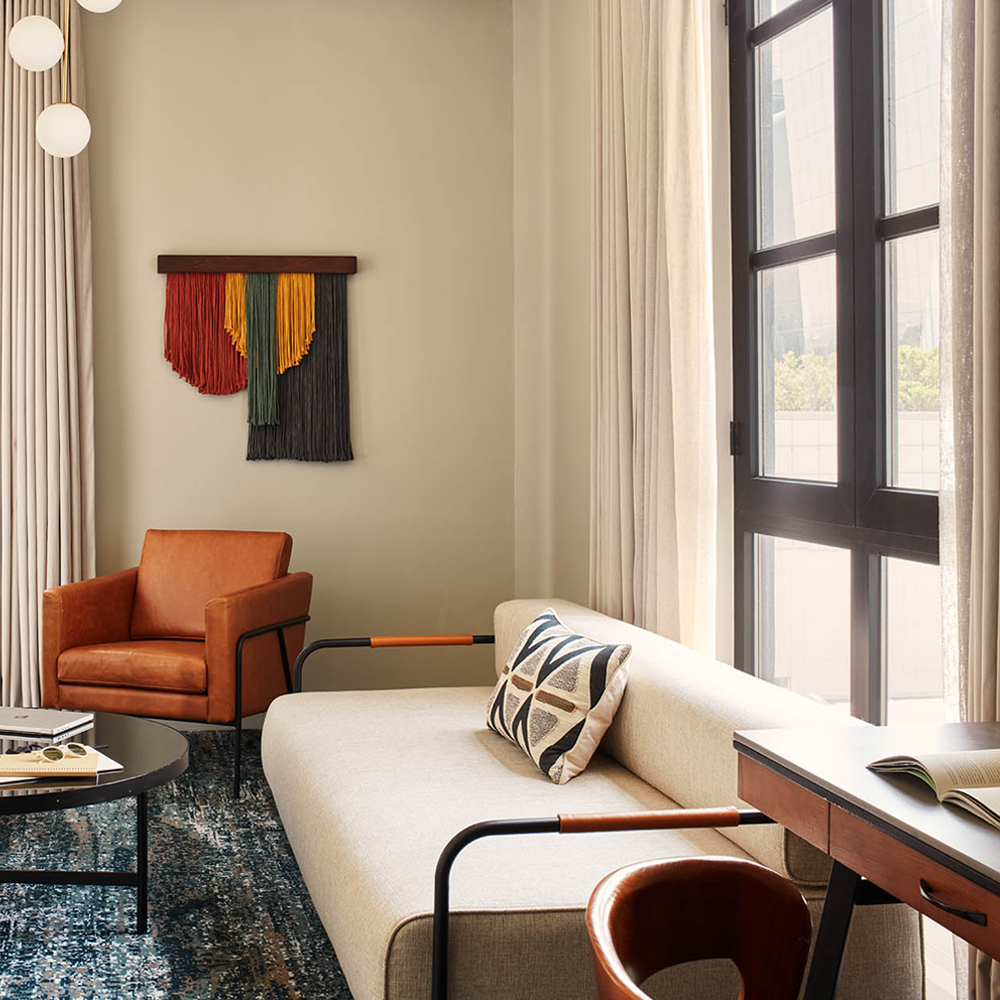 A 3-seater grey couch, with a 1-seater brown leather couch at the back, and hanging wall art.