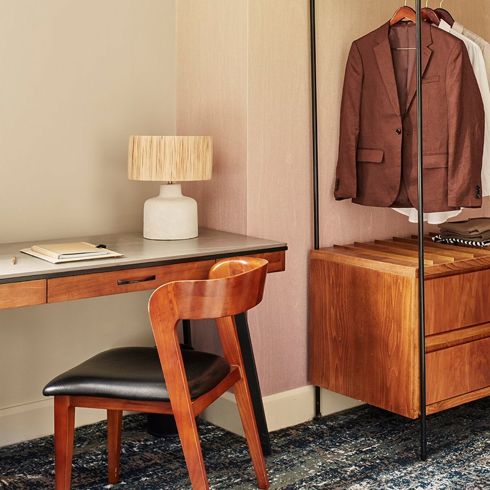A desk with a lamp which can be used for work or as a makeup area, and an open wardrobe with wooden drawers on the bottom.