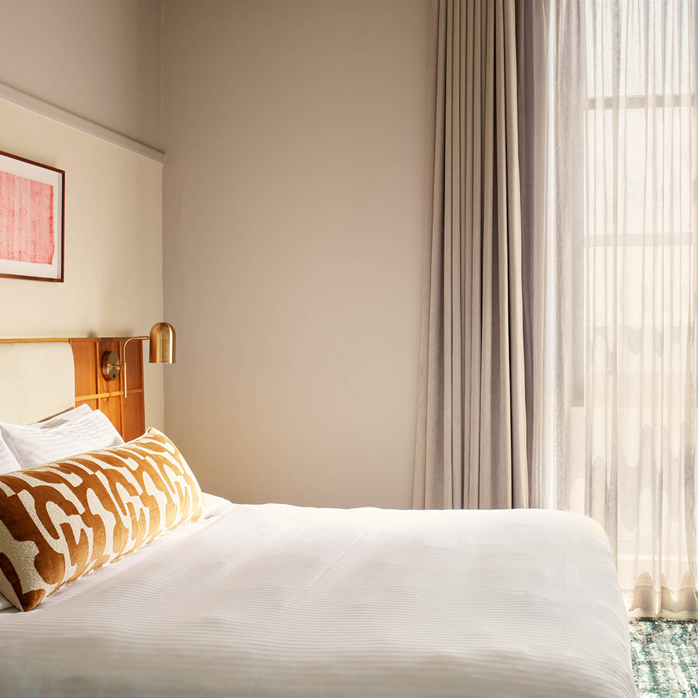 A king-sized bed with sunlight pouring through the sheer curtains.