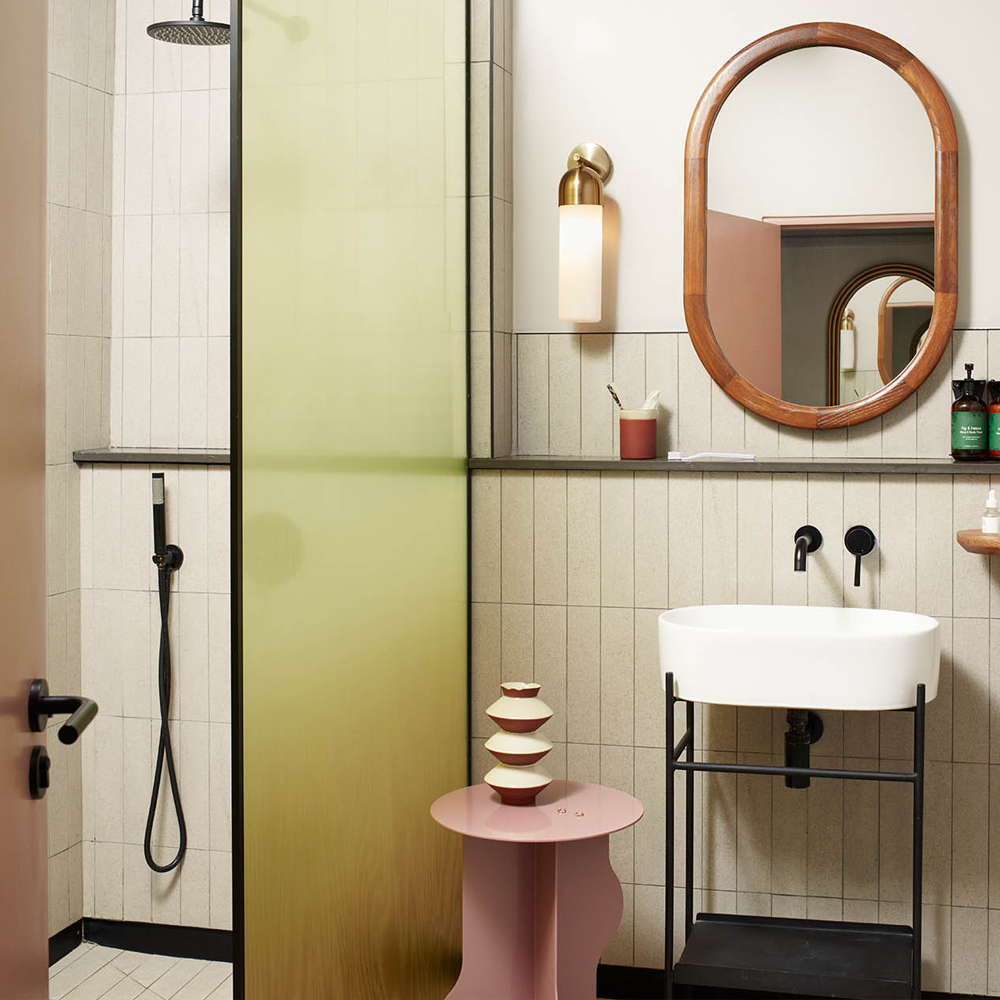 A walk-in shower to the left of the image, and the sink with a mirror on the right. There is also a knee-high pink table for additional space for accessories.