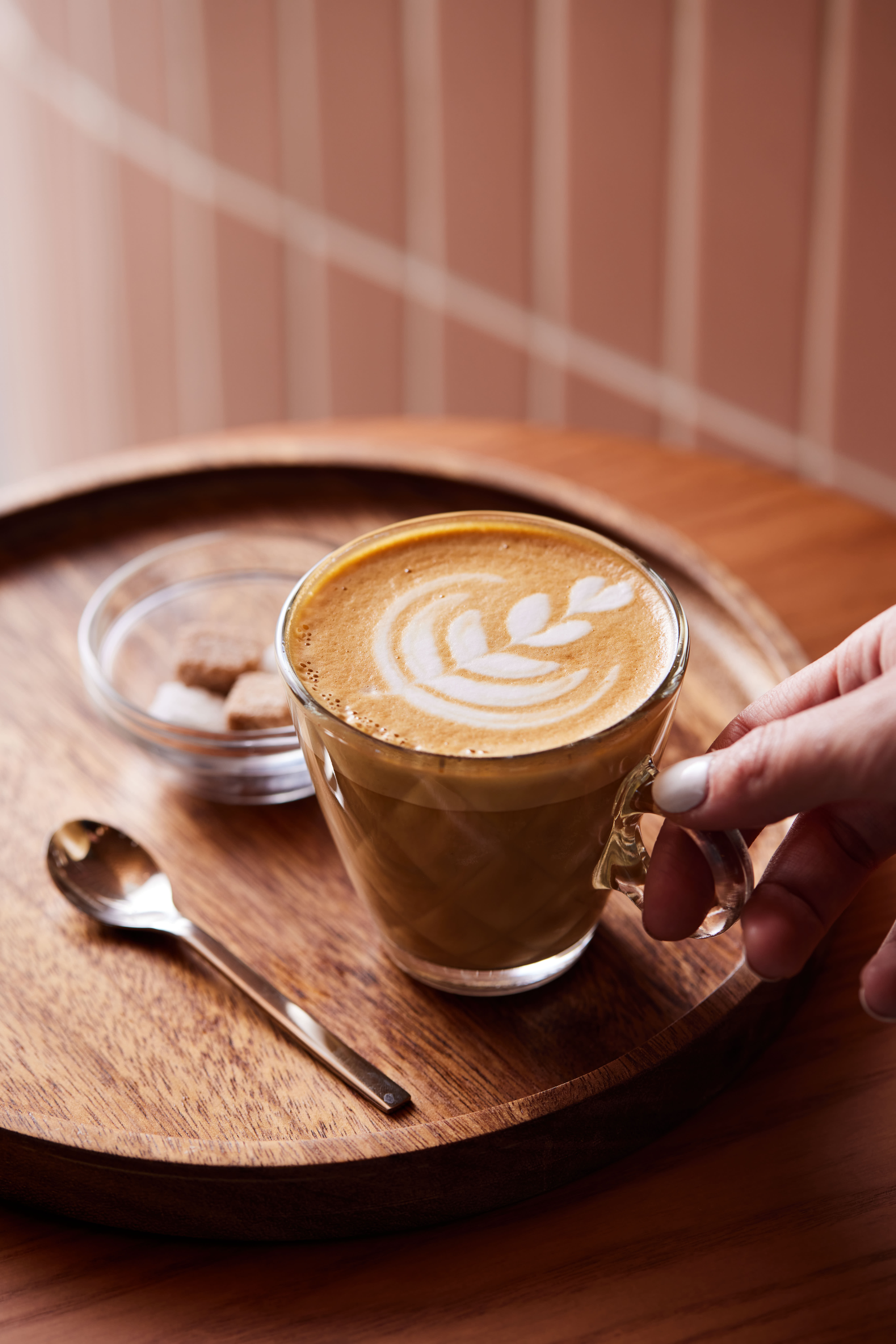 A hand holding a cup of coffee (latte) and a spoon
